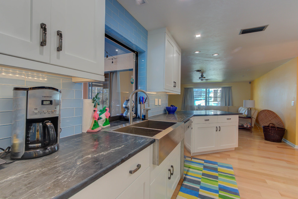 Photo of a mid-sized midcentury galley separate kitchen in Other with a farmhouse sink, shaker cabinets, white cabinets, soapstone benchtops, blue splashback, porcelain splashback, stainless steel appliances, light hardwood floors, a peninsula and brown floor.