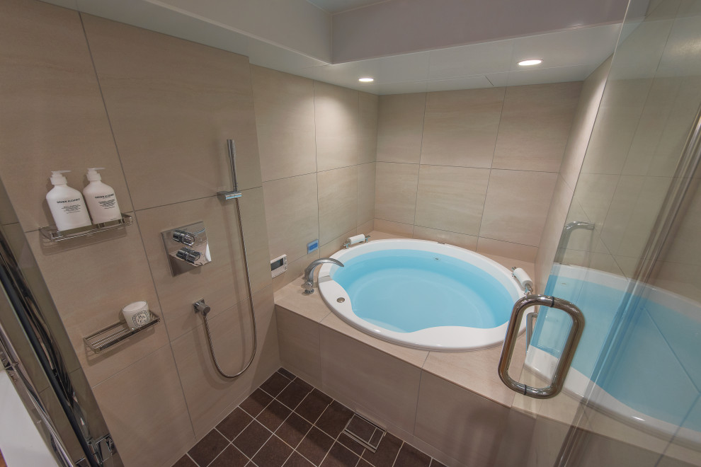 Photo of a bathroom with a hot tub, beige tile, porcelain tile, beige walls, cork floors and brown floor.