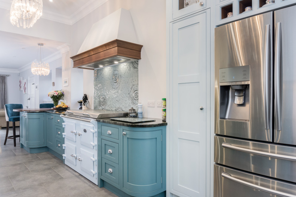 Пример оригинального дизайна: большая прямая кухня-гостиная со шкафом над холодильником в стиле неоклассика (современная классика) с накладной мойкой, фасадами с утопленной филенкой, синими фасадами, гранитной столешницей, цветной техникой, полом из керамической плитки, черной столешницей, синим фартуком, фартуком из стекла и серым полом