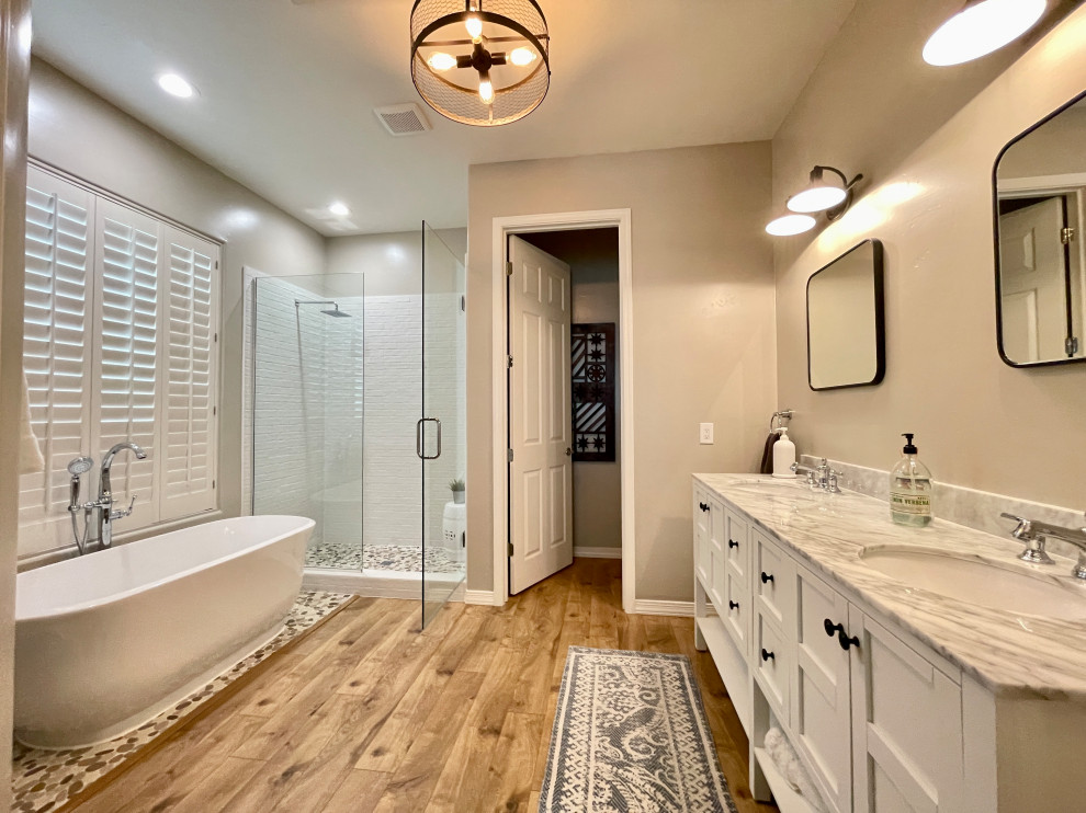 Inredning av ett klassiskt stort vit vitt en-suite badrum, med skåp i shakerstil, vita skåp, ett fristående badkar, en dusch i en alkov, vit kakel, porslinskakel, ett undermonterad handfat, marmorbänkskiva, dusch med gångjärnsdörr, en toalettstol med hel cisternkåpa, grå väggar, klinkergolv i porslin och brunt golv