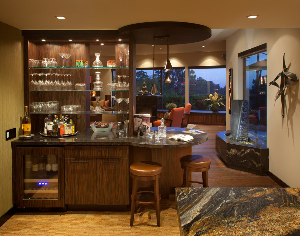 Design ideas for a mid-sized contemporary single-wall seated home bar in San Diego with no sink, flat-panel cabinets, dark wood cabinets, granite benchtops, mirror splashback, carpet and brown floor.