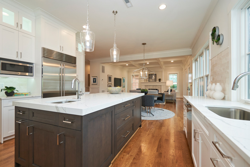 This is an example of a large transitional u-shaped eat-in kitchen in DC Metro with an undermount sink, shaker cabinets, white cabinets, quartz benchtops, white splashback, marble splashback, stainless steel appliances, medium hardwood floors, with island, brown floor and white benchtop.