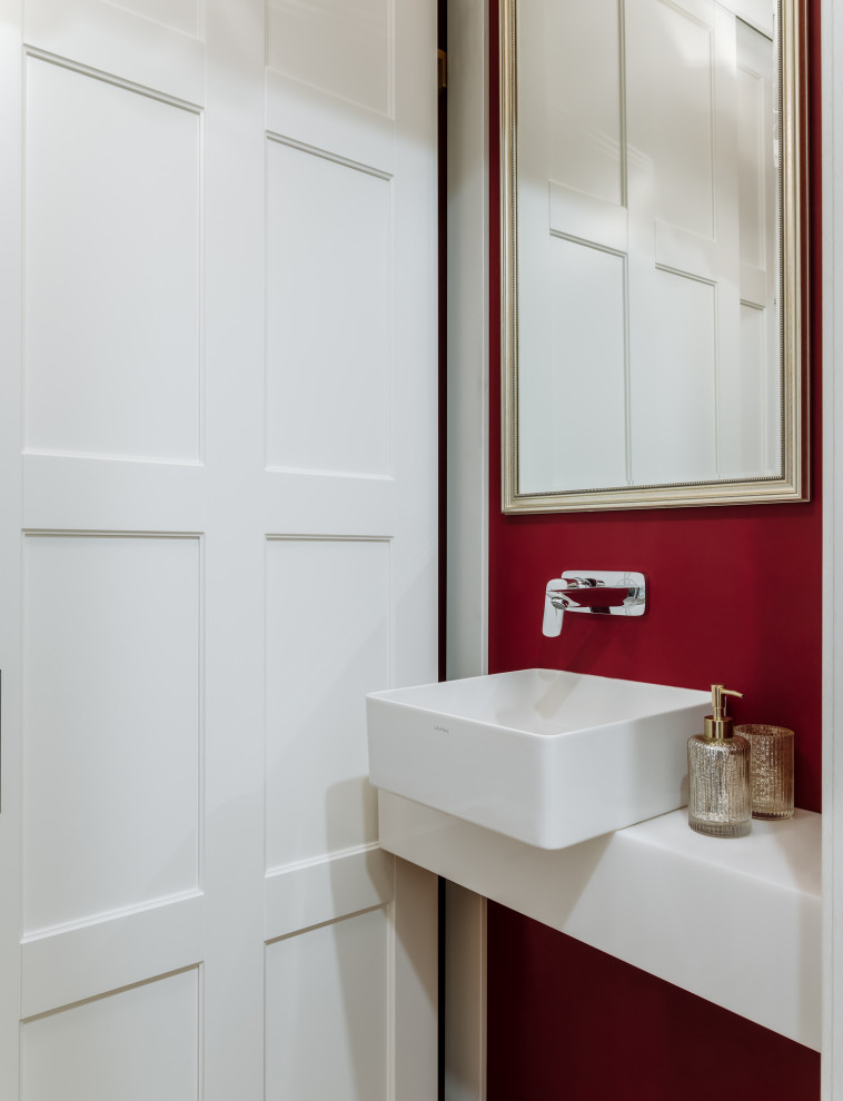 Inredning av ett klassiskt litet vit vitt toalett, med luckor med upphöjd panel, vita skåp, en vägghängd toalettstol, röda väggar, mellanmörkt trägolv, ett nedsänkt handfat, bänkskiva i akrylsten och gult golv
