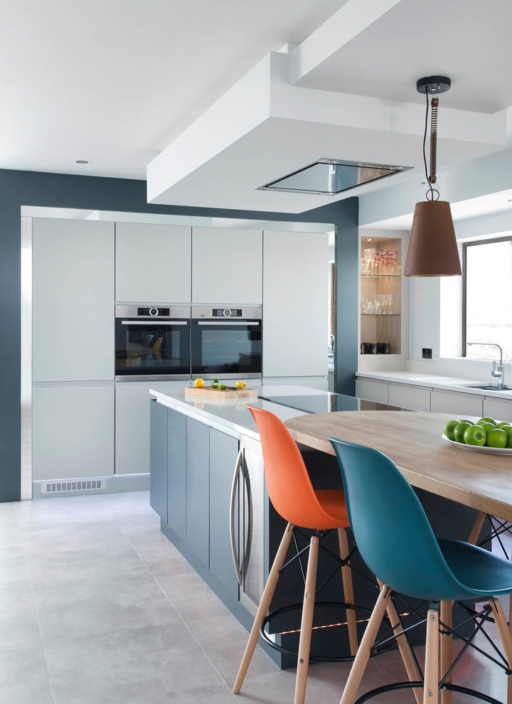 Photo of a contemporary kitchen/diner with blue cabinets, coloured appliances, an island and grey floors.