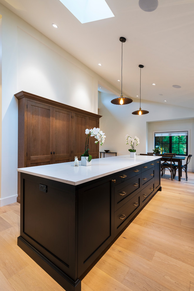 Open concept kitchen - mid-sized rustic l-shaped light wood floor and beige floor open concept kitchen idea in Vancouver with a farmhouse sink, shaker cabinets, black cabinets, quartz countertops, paneled appliances, an island and white countertops