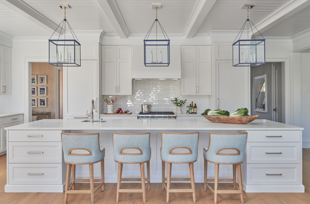 Inspiration for a beach style l-shaped eat-in kitchen in Boston with an undermount sink, recessed-panel cabinets, white cabinets, quartzite benchtops, white splashback, ceramic splashback, stainless steel appliances, light hardwood floors, with island, brown floor, white benchtop and timber.