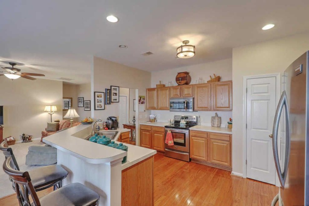 Example of a mid-sized u-shaped medium tone wood floor and brown floor kitchen design in Charleston with an undermount sink, raised-panel cabinets, beige cabinets, granite countertops, brown backsplash, ceramic backsplash, stainless steel appliances and beige countertops