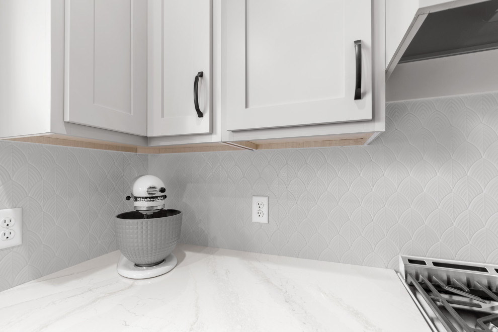 Example of a mid-sized transitional l-shaped light wood floor and beige floor kitchen design in Minneapolis with an undermount sink, shaker cabinets, white cabinets, quartz countertops, white backsplash, ceramic backsplash, stainless steel appliances, an island and white countertops