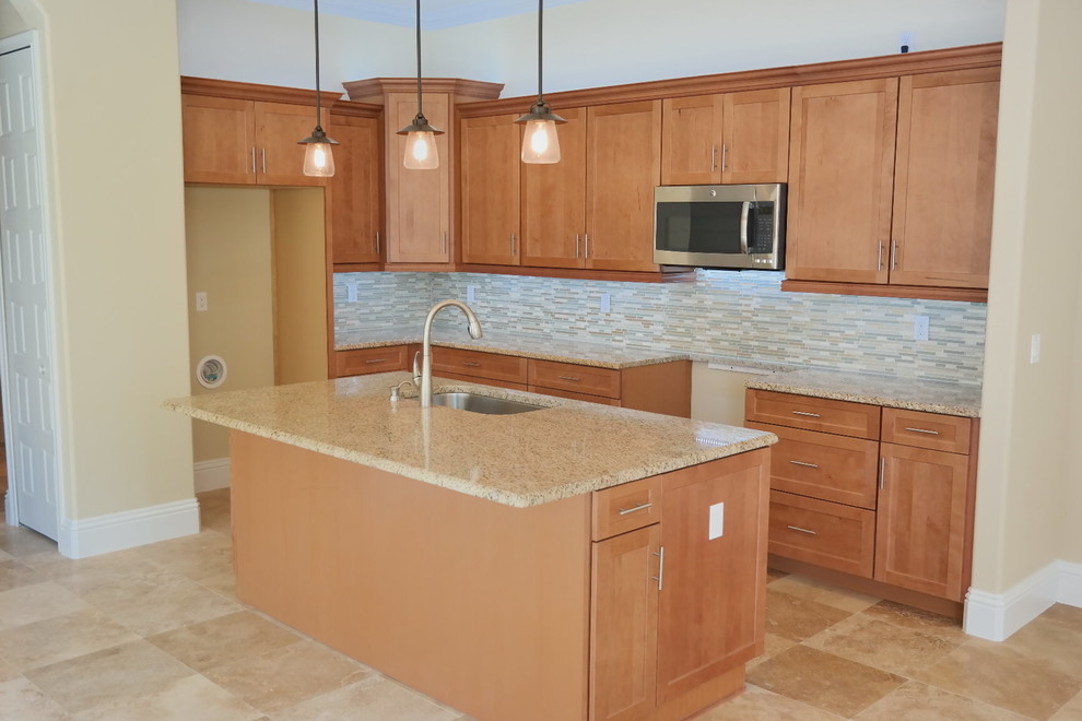 This is an example of an arts and crafts kitchen in Miami with a single-bowl sink, shaker cabinets, medium wood cabinets, granite benchtops, beige splashback, glass sheet splashback, stainless steel appliances, travertine floors and with island.