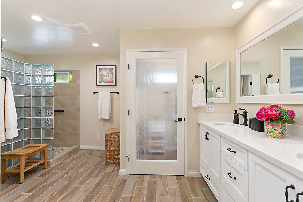 This is an example of a mid-sized transitional master bathroom in San Diego with recessed-panel cabinets, white cabinets, a corner shower, beige tile, beige walls, ceramic floors, an undermount sink, engineered quartz benchtops, beige floor, an open shower and white benchtops.