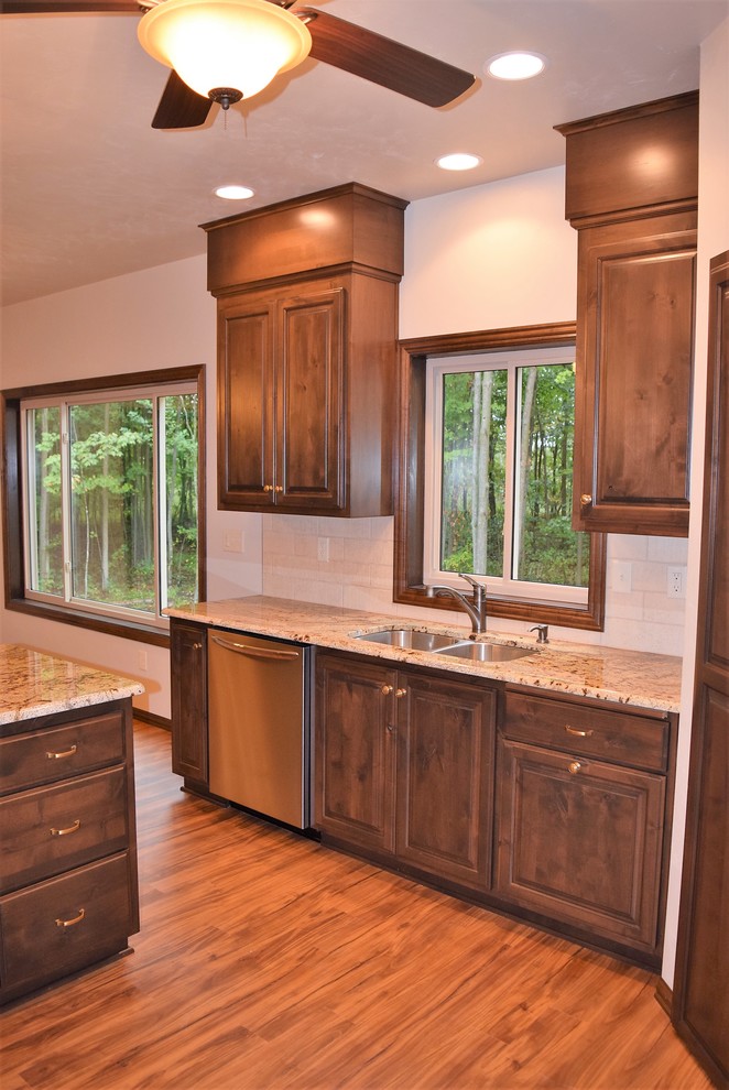 Light wood floor open concept kitchen photo with an undermount sink, raised-panel cabinets, dark wood cabinets, granite countertops, white backsplash, ceramic backsplash, stainless steel appliances and an island
