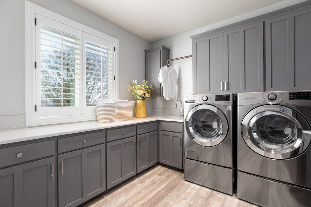 Large transitional u-shaped dedicated laundry room in Portland with an undermount sink, shaker cabinets, grey cabinets, quartz benchtops, white splashback, mosaic tile splashback, grey walls, vinyl floors, a side-by-side washer and dryer, brown floor and white benchtop.