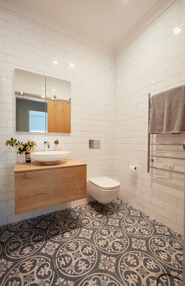 Small contemporary master bathroom in Sydney with medium wood cabinets, a freestanding tub, a shower/bathtub combo, a wall-mount toilet, blue tile, ceramic tile, white walls, ceramic floors, a vessel sink, wood benchtops and brown benchtops.