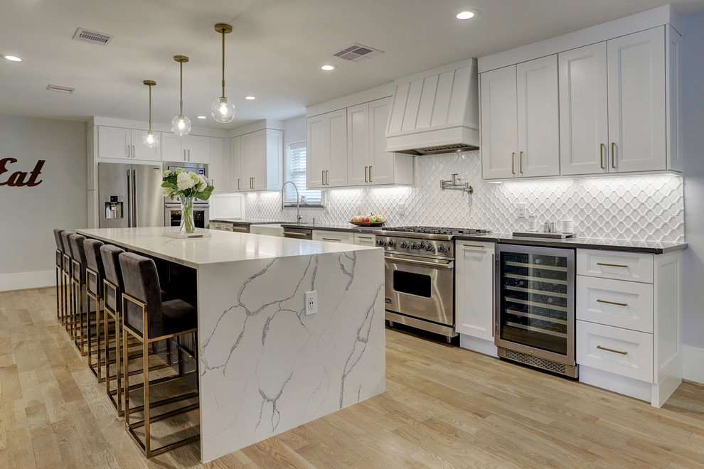 Design ideas for a mid-sized transitional l-shaped eat-in kitchen in Houston with a farmhouse sink, recessed-panel cabinets, white cabinets, quartz benchtops, white splashback, ceramic splashback, stainless steel appliances, light hardwood floors, with island, white benchtop and beige floor.