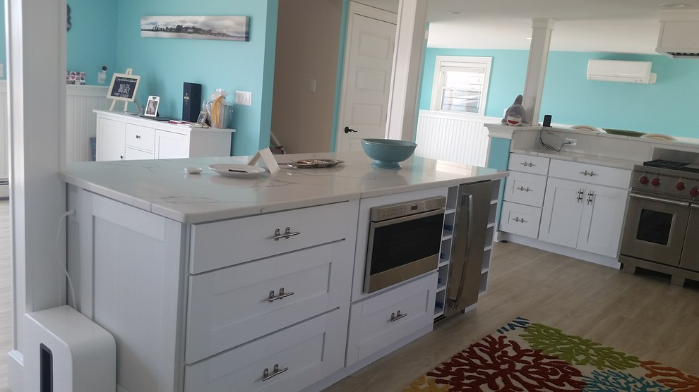 Design ideas for a large beach style l-shaped open plan kitchen in Boston with a farmhouse sink, recessed-panel cabinets, white cabinets, stainless steel appliances, light hardwood floors and with island.