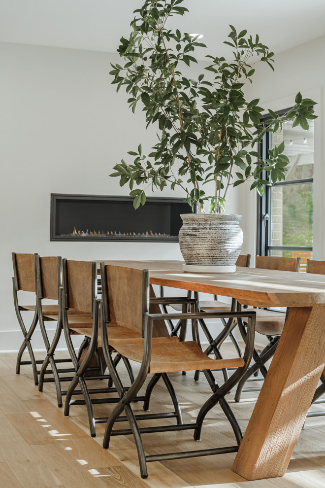 Immagine di una sala da pranzo aperta verso la cucina minimalista di medie dimensioni con pareti bianche, parquet chiaro, camino lineare Ribbon, cornice del camino in metallo e pavimento marrone