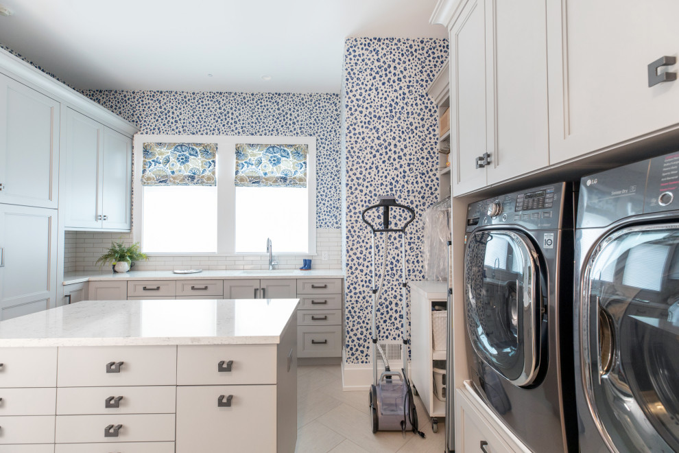 Photo of a medium sized modern u-shaped separated utility room in Milwaukee with a submerged sink, flat-panel cabinets, white cabinets, engineered stone countertops, white splashback, cement tile splashback, blue walls, porcelain flooring, a side by side washer and dryer, beige floors, white worktops and wallpapered walls.