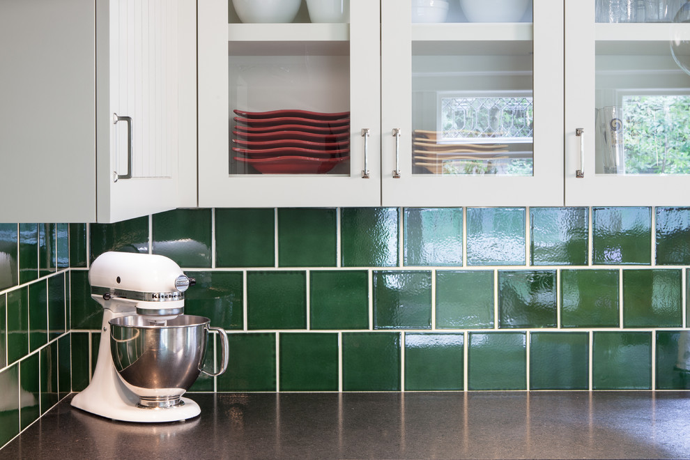 Inspiration for a mid-sized traditional l-shaped separate kitchen in Portland with a farmhouse sink, glass-front cabinets, white cabinets, granite benchtops, green splashback, ceramic splashback, stainless steel appliances, light hardwood floors and with island.