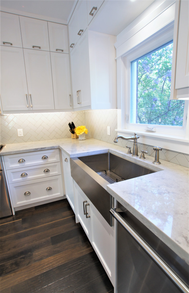 Large transitional l-shaped dark wood floor and brown floor eat-in kitchen photo in Toronto with a farmhouse sink, shaker cabinets, white cabinets, quartz countertops, gray backsplash, subway tile backsplash, stainless steel appliances, an island and gray countertops