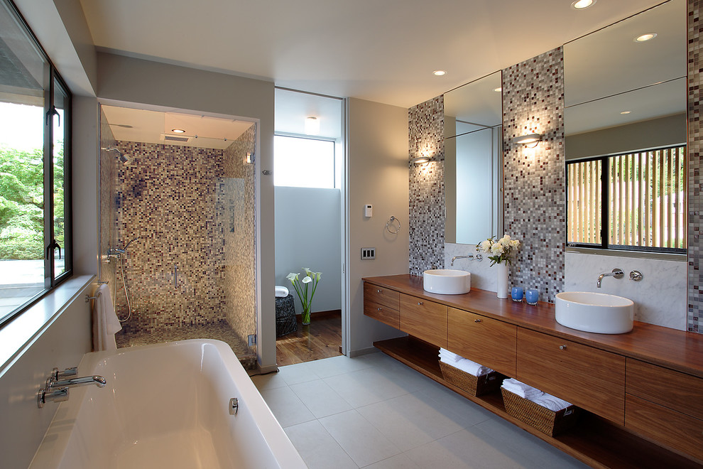 Inspiration for a contemporary master bathroom in Seattle with a vessel sink, flat-panel cabinets, medium wood cabinets, wood benchtops, a freestanding tub, an alcove shower, multi-coloured tile, white walls and porcelain floors.