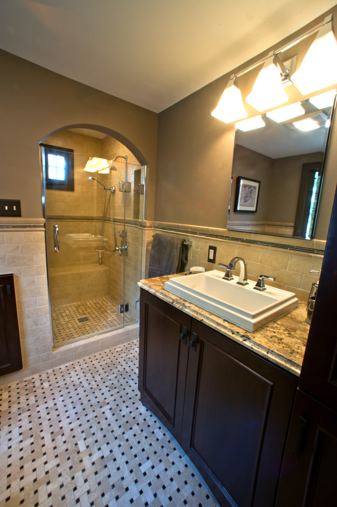 Photo of a mid-sized traditional bathroom in Milwaukee with a drop-in sink, beaded inset cabinets, dark wood cabinets, granite benchtops, an alcove shower, a two-piece toilet, beige tile, ceramic tile and brown walls.