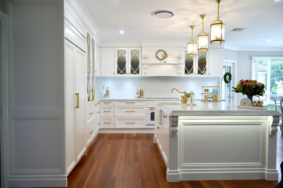 Idéer för stora vintage grått kök, med en rustik diskho, luckor med infälld panel, vita skåp, marmorbänkskiva, vitt stänkskydd, stänkskydd i keramik, vita vitvaror, mellanmörkt trägolv, en köksö och brunt golv