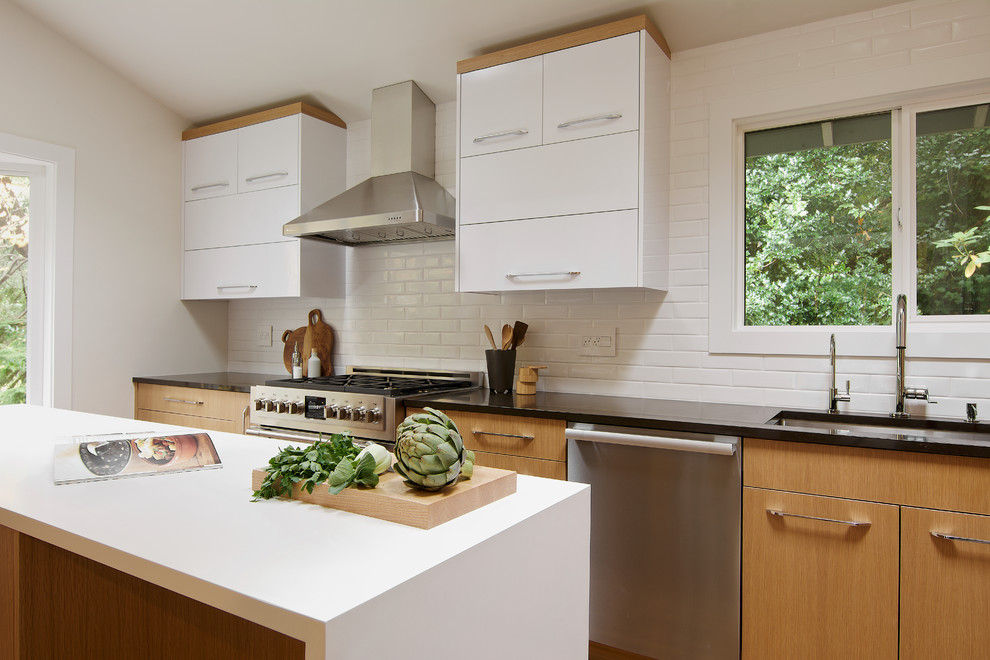Photo of a small modern l-shaped separate kitchen in Seattle with a single-bowl sink, flat-panel cabinets, light wood cabinets, quartz benchtops, white splashback, ceramic splashback, stainless steel appliances, light hardwood floors, with island and brown floor.