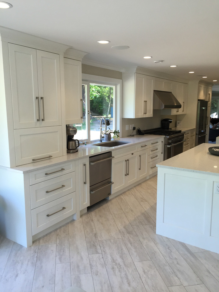 This is an example of a large transitional single-wall eat-in kitchen in Vancouver with an undermount sink, shaker cabinets, white cabinets, quartz benchtops, stainless steel appliances, laminate floors, with island and beige floor.