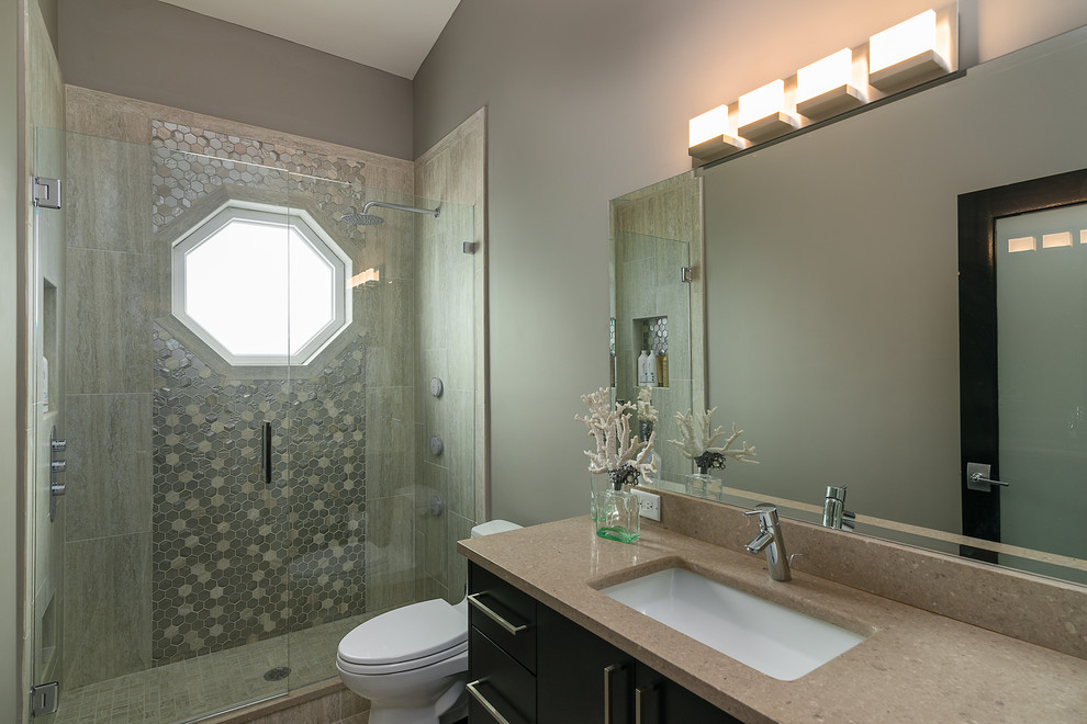 Inspiration for a mid-sized beach style 3/4 bathroom in Tampa with flat-panel cabinets, black cabinets, a two-piece toilet, gray tile, grey walls, porcelain floors, an undermount sink, engineered quartz benchtops, an alcove shower, mosaic tile and a sliding shower screen.