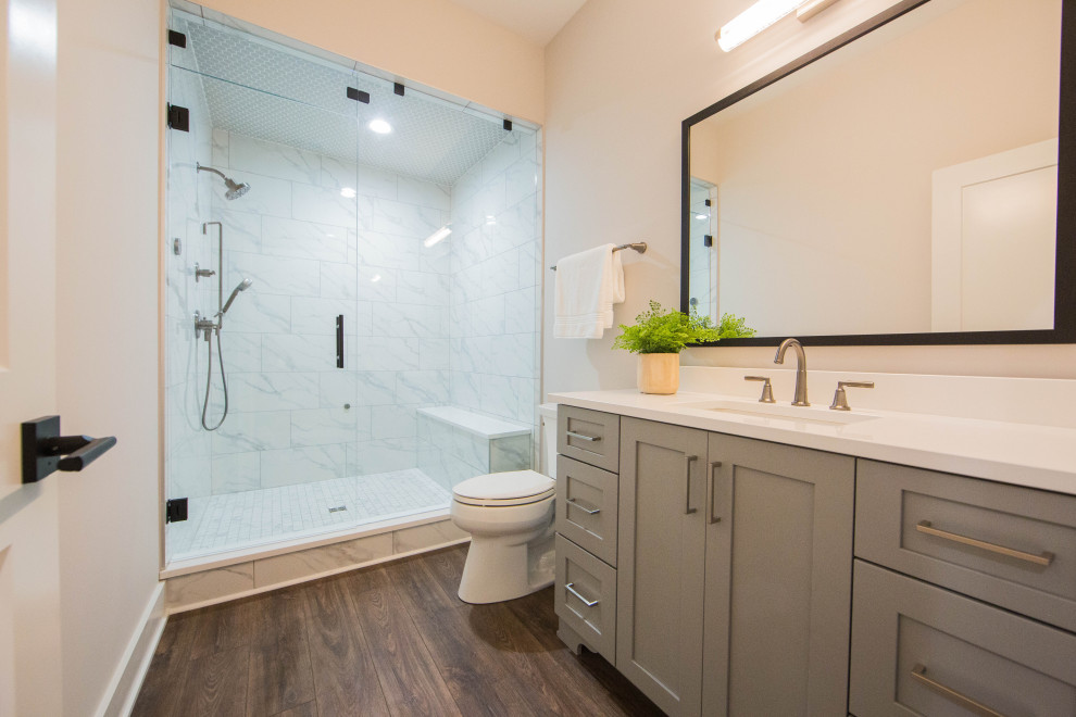 Huge minimalist white tile and stone tile medium tone wood floor, brown floor and single-sink bathroom photo in Indianapolis with recessed-panel cabinets, gray cabinets, a two-piece toilet, white walls, an undermount sink, granite countertops, a hinged shower door, white countertops and a freestanding vanity