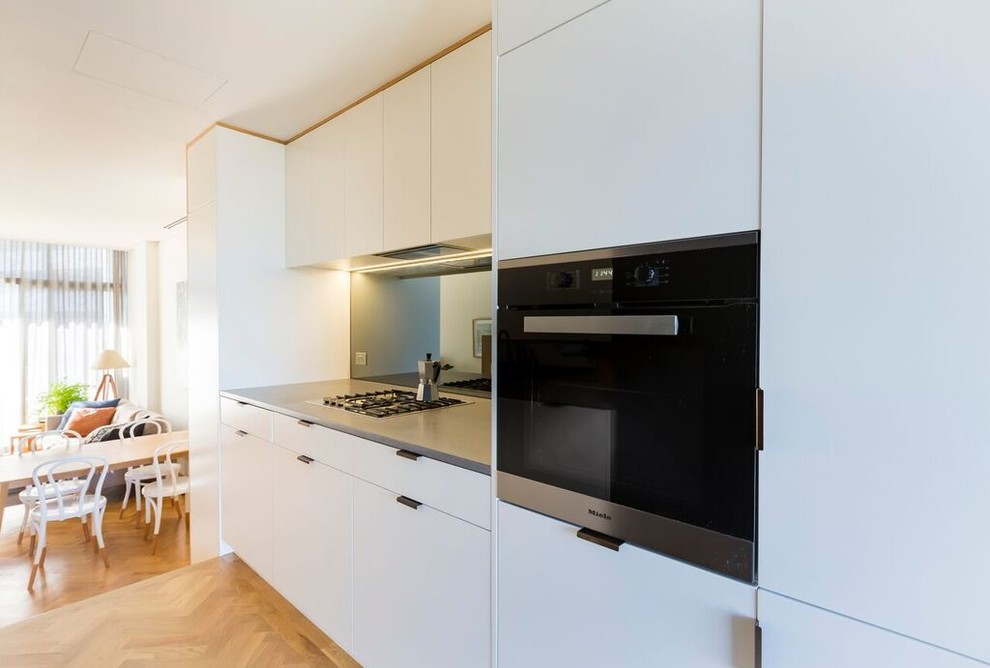 Photo of a small contemporary galley separate kitchen in Sydney with an undermount sink, flat-panel cabinets, white cabinets, concrete benchtops, grey splashback, glass sheet splashback, stainless steel appliances, light hardwood floors, no island and yellow floor.