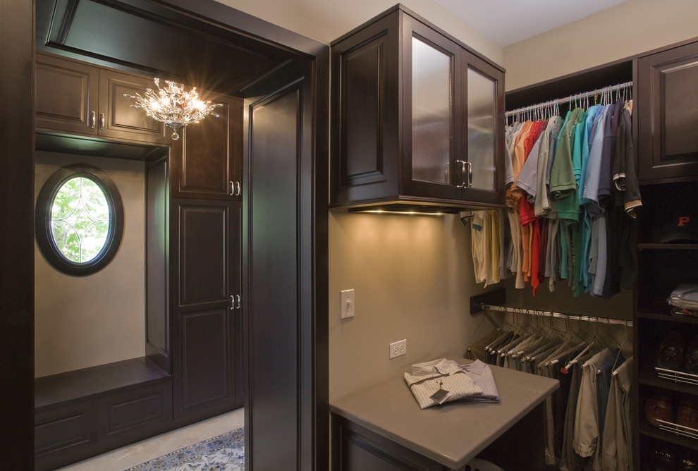 Large traditional gender-neutral dressing room in Chicago with raised-panel cabinets, dark wood cabinets, limestone floors and beige floor.