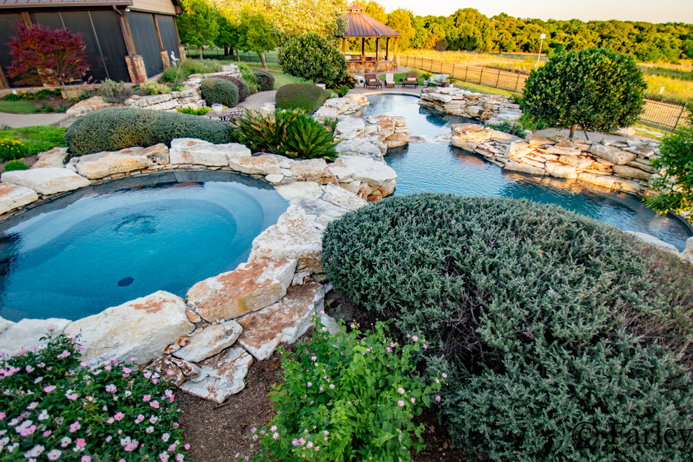 Expansive country backyard custom-shaped natural pool in Dallas with a water feature and natural stone pavers.