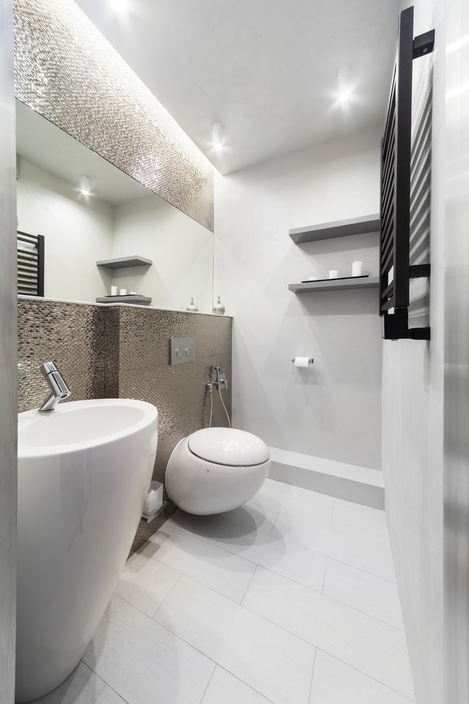 This is an example of a mid-sized contemporary powder room in Yekaterinburg with a wall-mount toilet, gray tile, white walls and a pedestal sink.