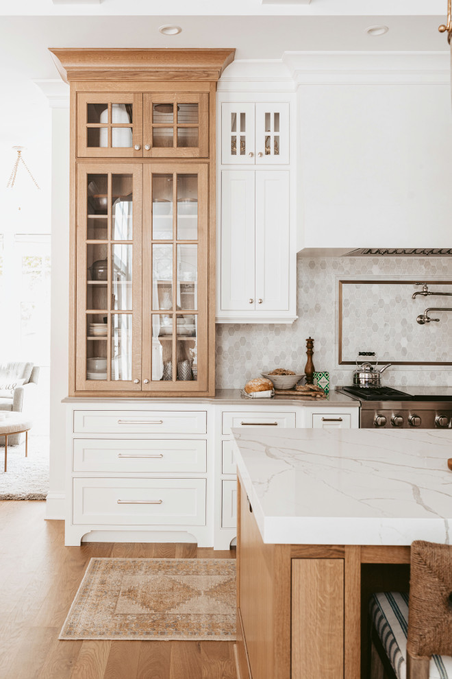 Grand Haven Custom Home - The grand white kitchen is warmed up by select white oak stained island and display cabinet. Quartz cabinets, marble  mosaic backsplash with hints of soft antique brass finishes.
