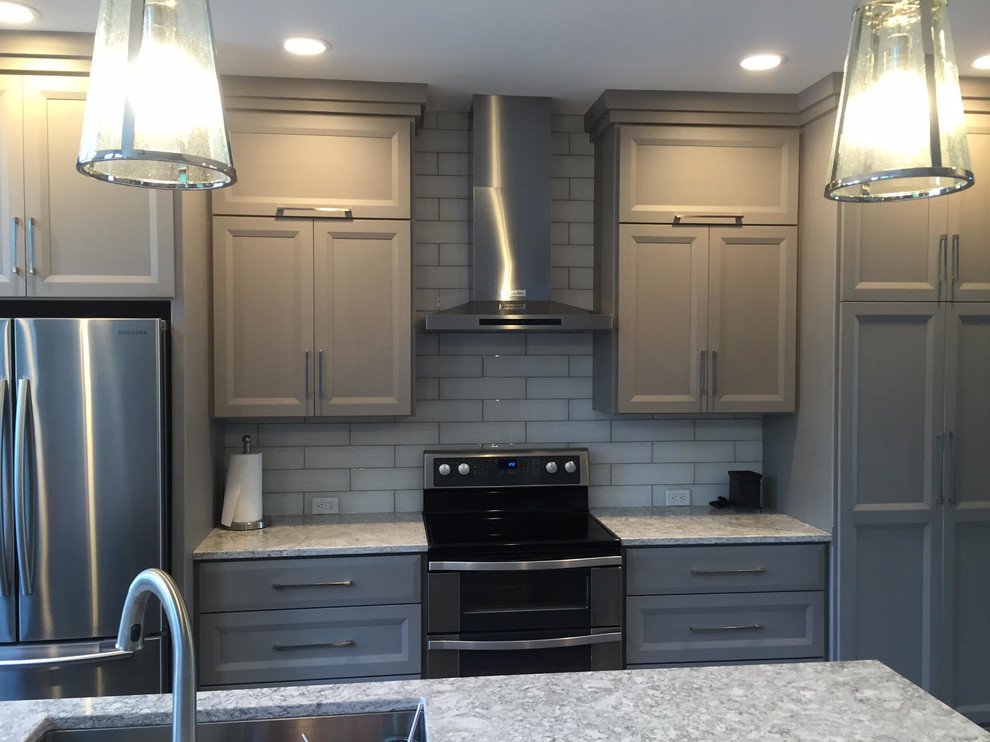 Eat-in kitchen - mid-sized transitional l-shaped medium tone wood floor eat-in kitchen idea in Cedar Rapids with a double-bowl sink, recessed-panel cabinets, gray cabinets, quartz countertops, white backsplash, glass tile backsplash, stainless steel appliances and an island