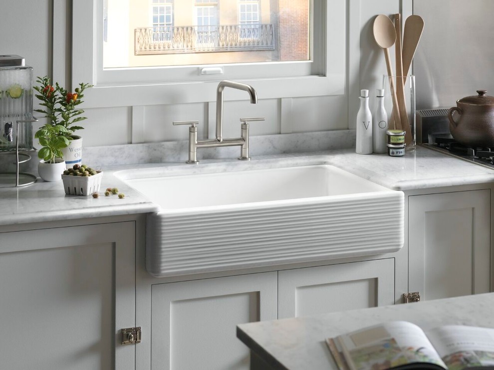 Example of a transitional l-shaped eat-in kitchen design in Providence with a farmhouse sink, recessed-panel cabinets, white cabinets, solid surface countertops, white backsplash, ceramic backsplash and an island