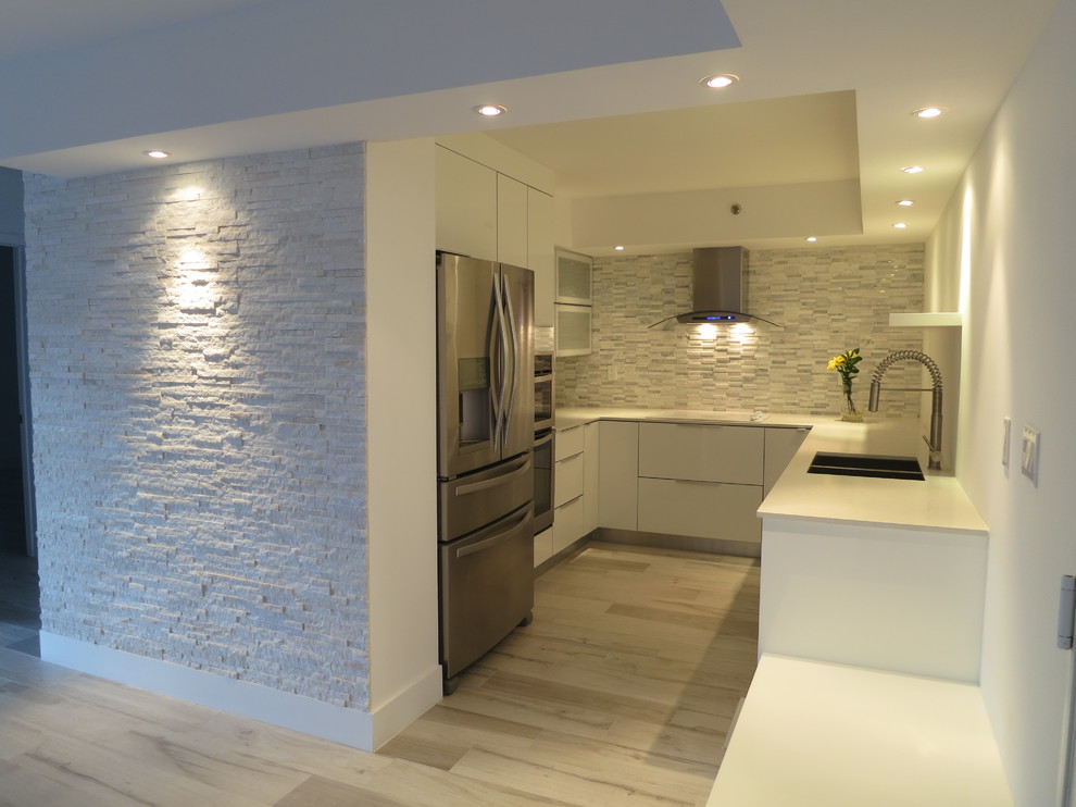 Inspiration for a small modern u-shaped separate kitchen in Miami with a double-bowl sink, flat-panel cabinets, white cabinets, marble benchtops, white splashback, ceramic splashback, stainless steel appliances and bamboo floors.