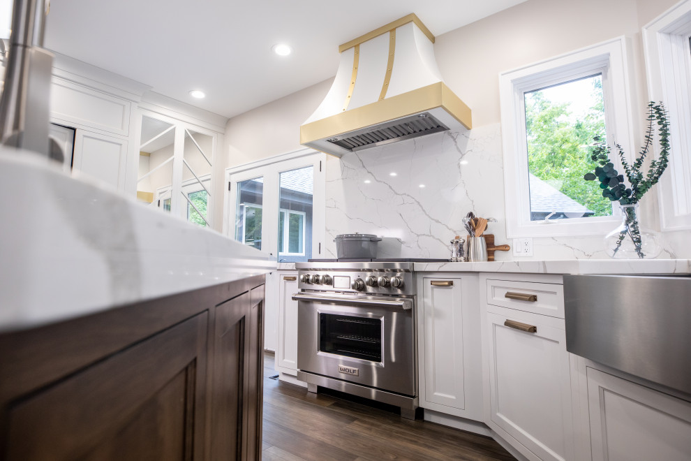 Transitional medium tone wood floor and brown floor eat-in kitchen photo with a farmhouse sink, shaker cabinets, white cabinets, quartz countertops, white backsplash, quartz backsplash, stainless steel appliances, two islands and white countertops