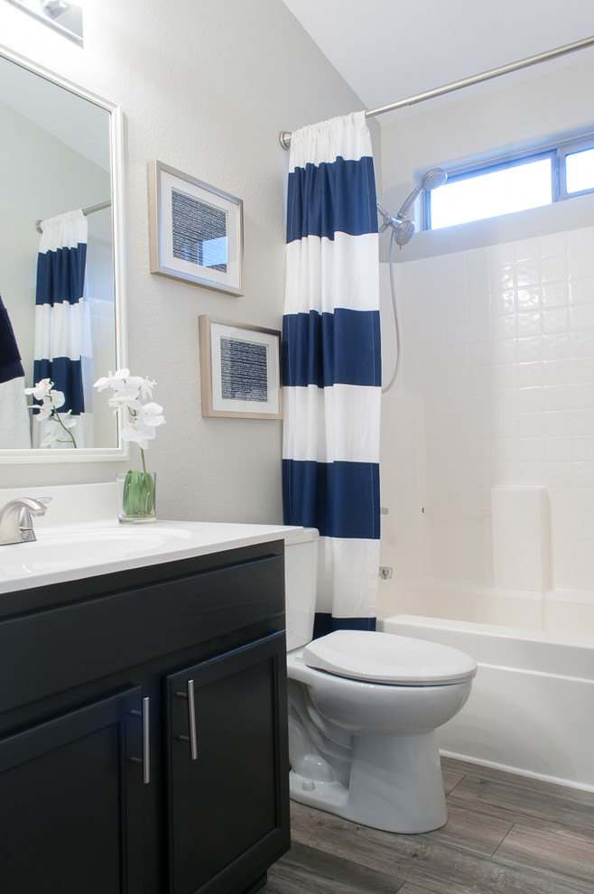 Inspiration for a small transitional bathroom in Phoenix with shaker cabinets, black cabinets, a drop-in tub, a shower/bathtub combo, white tile, grey walls and vinyl floors.