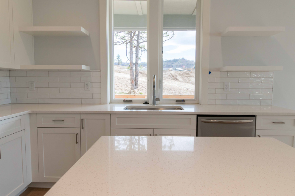 Photo of a mid-sized contemporary eat-in kitchen in Other with an undermount sink, shaker cabinets, white cabinets, quartz benchtops, white splashback, ceramic splashback, stainless steel appliances, medium hardwood floors, with island and white benchtop.