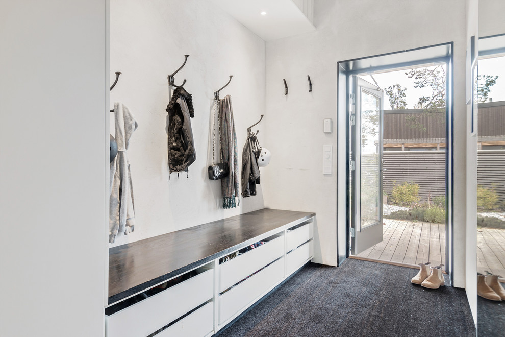 This is an example of a mid-sized scandinavian mudroom in Stockholm with white walls, carpet and black floor.