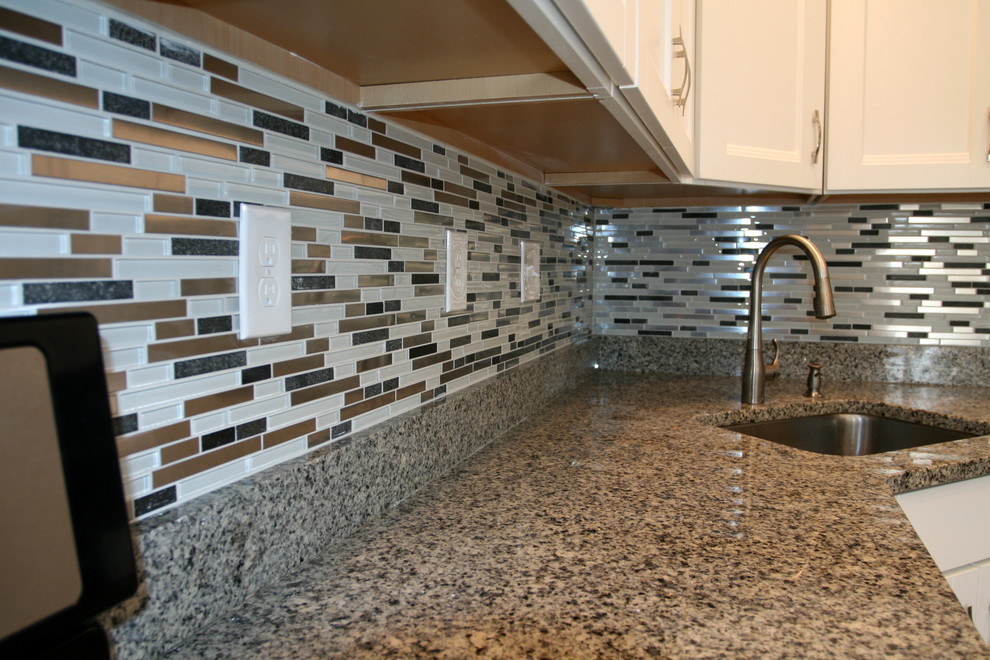 Example of a mid-sized minimalist medium tone wood floor kitchen design in Baltimore with an undermount sink, white cabinets, granite countertops, multicolored backsplash, glass tile backsplash and stainless steel appliances