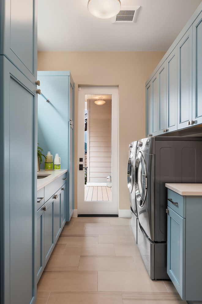 Inspiration for a mid-sized transitional galley utility room in Seattle with an undermount sink, blue cabinets, quartz benchtops, beige walls, a side-by-side washer and dryer, white benchtop, shaker cabinets and beige floor.