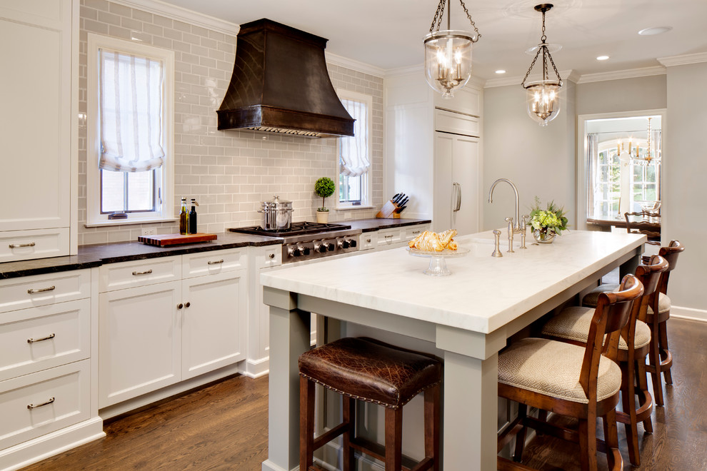 Design ideas for a traditional galley kitchen in Milwaukee with an undermount sink, recessed-panel cabinets, white cabinets, grey splashback, subway tile splashback, stainless steel appliances, dark hardwood floors and with island.