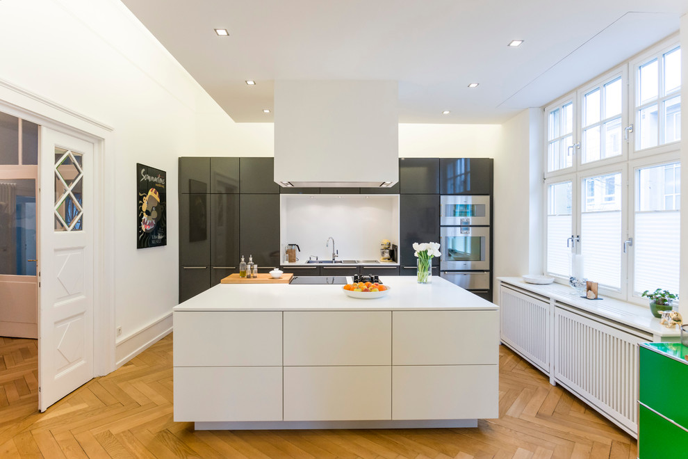 Inspiration for a mid-sized contemporary separate kitchen in Berlin with a drop-in sink, flat-panel cabinets, grey cabinets, panelled appliances, medium hardwood floors, with island and white splashback.