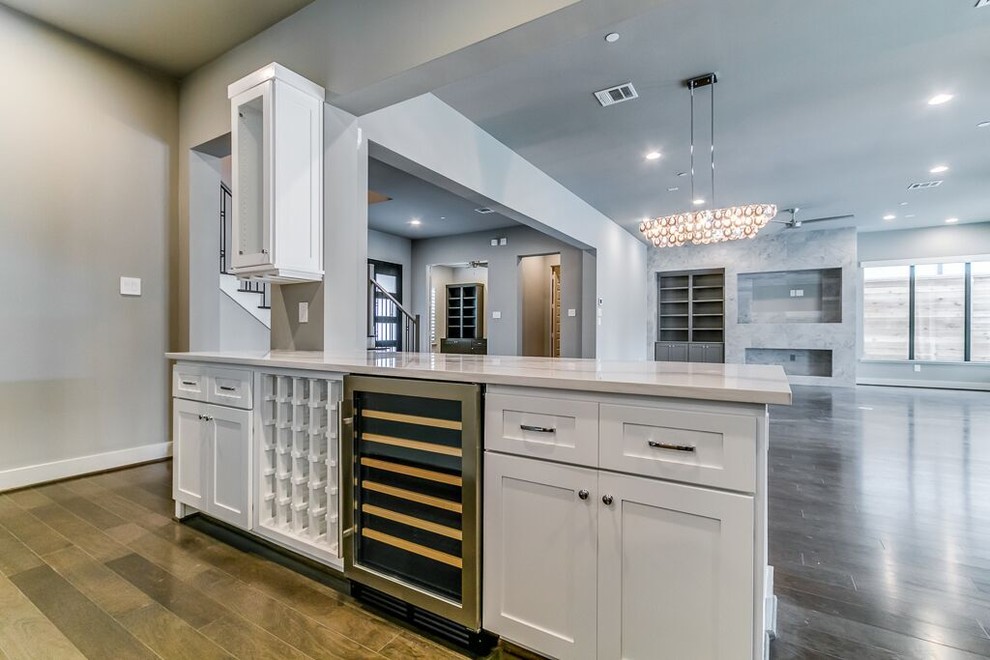 Inspiration for a transitional l-shaped brown floor open concept kitchen remodel in Houston with a farmhouse sink, shaker cabinets, white cabinets, quartz countertops, beige backsplash, subway tile backsplash, stainless steel appliances and an island