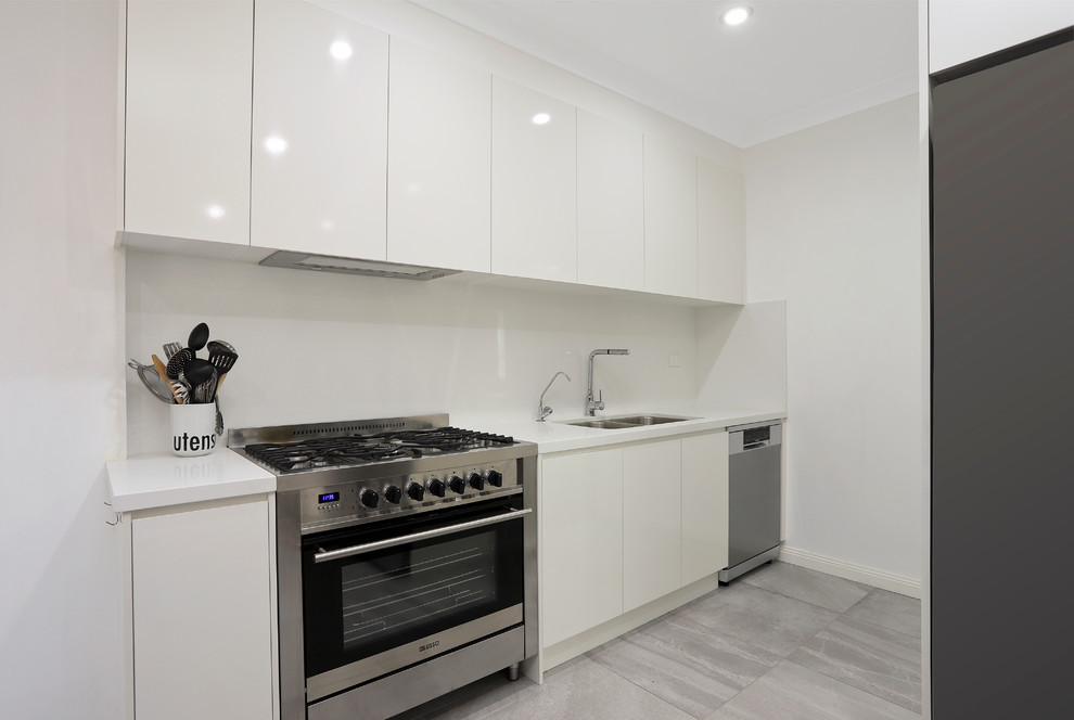 Photo of a mid-sized modern l-shaped eat-in kitchen in Sydney with an undermount sink, flat-panel cabinets, white cabinets, quartz benchtops, white splashback, slate splashback, stainless steel appliances, porcelain floors, no island, grey floor and white benchtop.