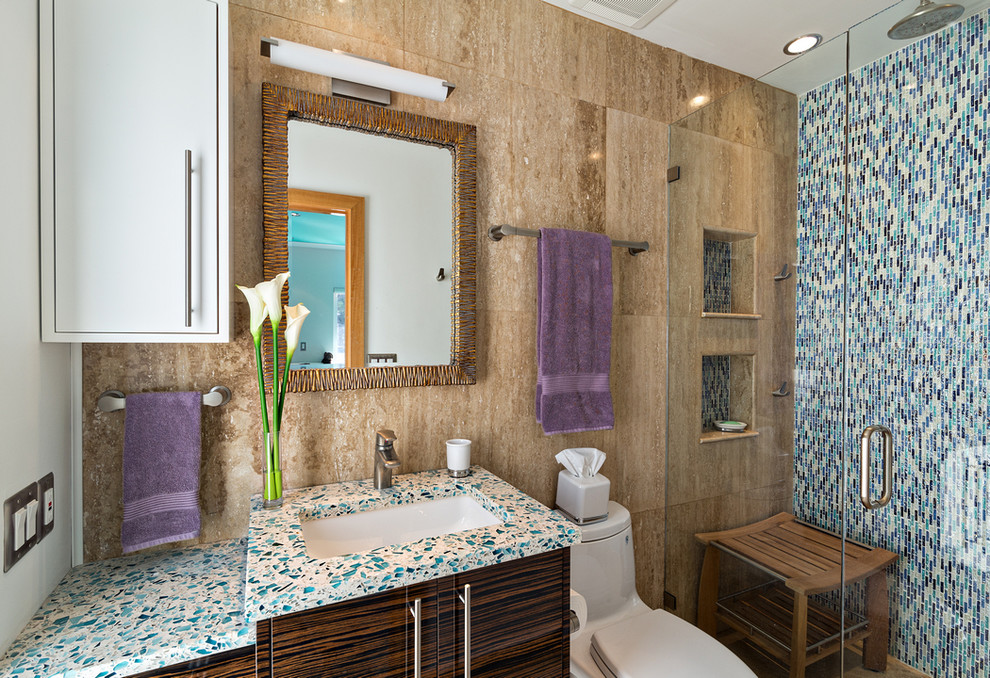 This is an example of a mid-sized tropical bathroom in Miami with flat-panel cabinets, dark wood cabinets, a curbless shower, a one-piece toilet, black tile, blue tile, green tile, multi-coloured tile, mosaic tile, brown walls, an undermount sink and recycled glass benchtops.