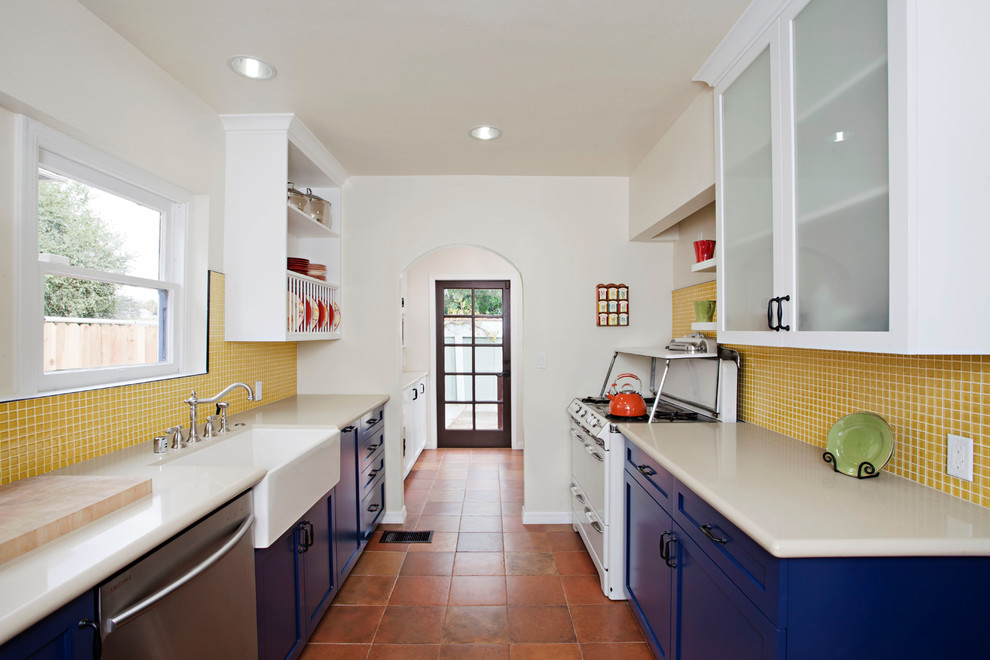 Mid-sized eclectic galley separate kitchen in Los Angeles with a farmhouse sink, shaker cabinets, blue cabinets, yellow splashback, mosaic tile splashback, white appliances, terra-cotta floors, brown floor and no island.